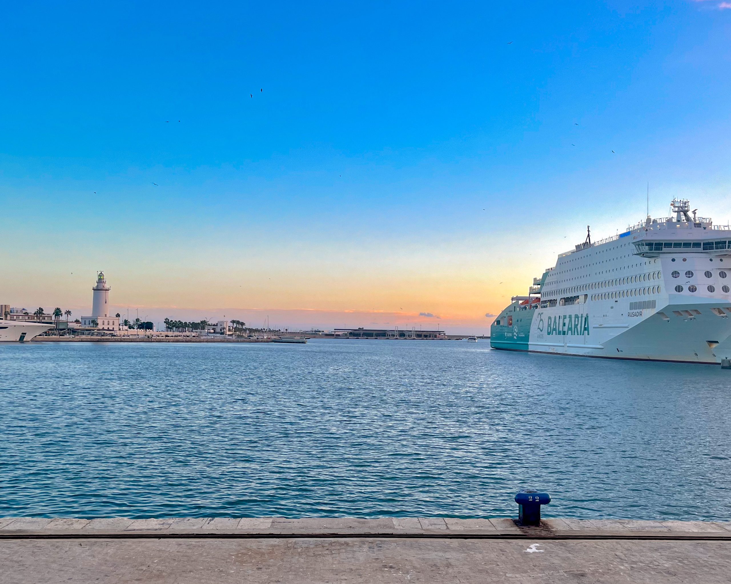 El puerto de Málaga con el crucero Balearia visto desde el Muelle Uno, con el faro de Farola al fondo, al atardecer