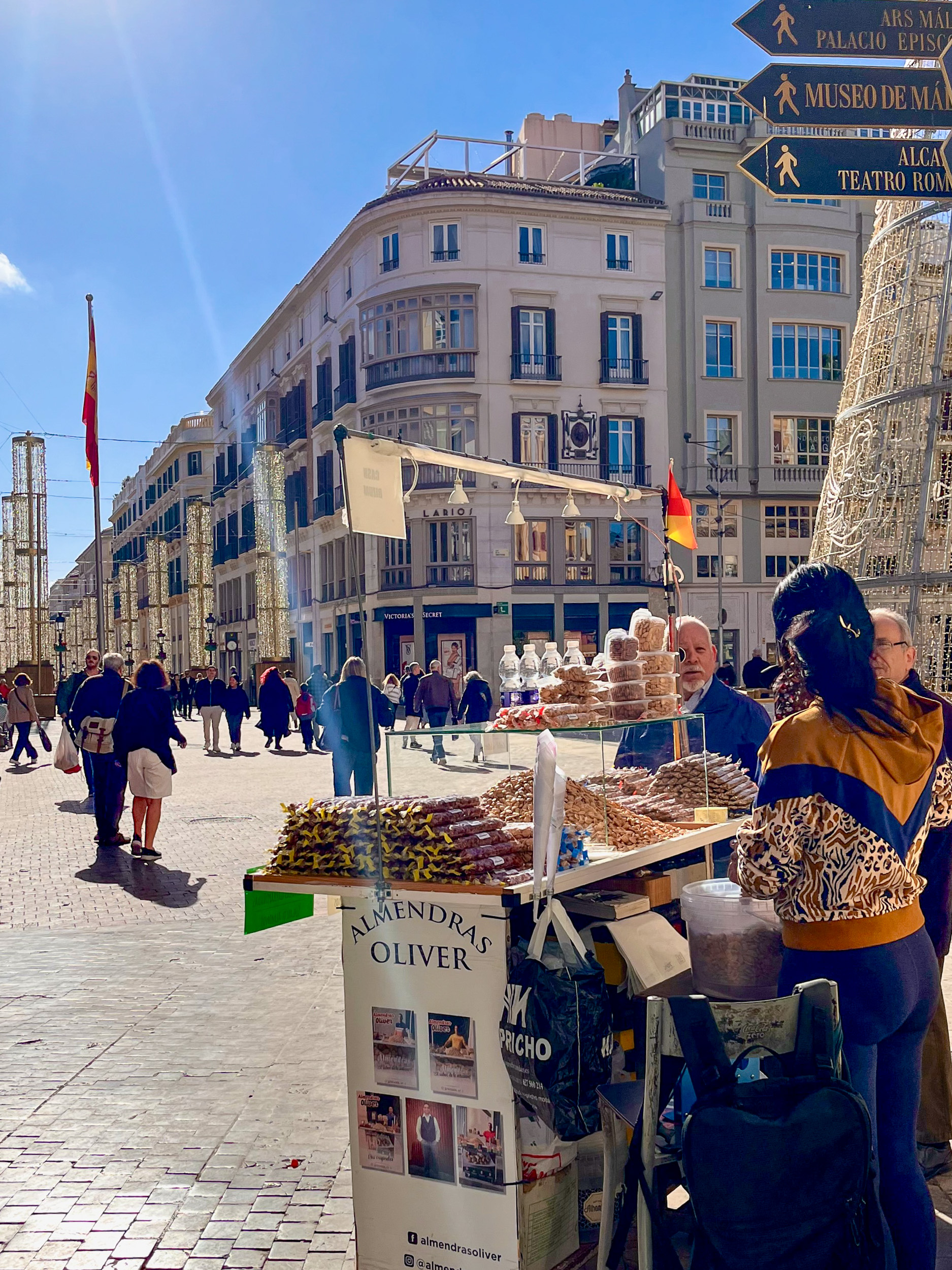El puesto de almendras Oliver en la esquina de la calle Granada y la Plaza de la Constitución, vendiendo almendras en la calle con la calle Marqués de Larios al fondo, en el centro histórico de la ciudad de Málaga