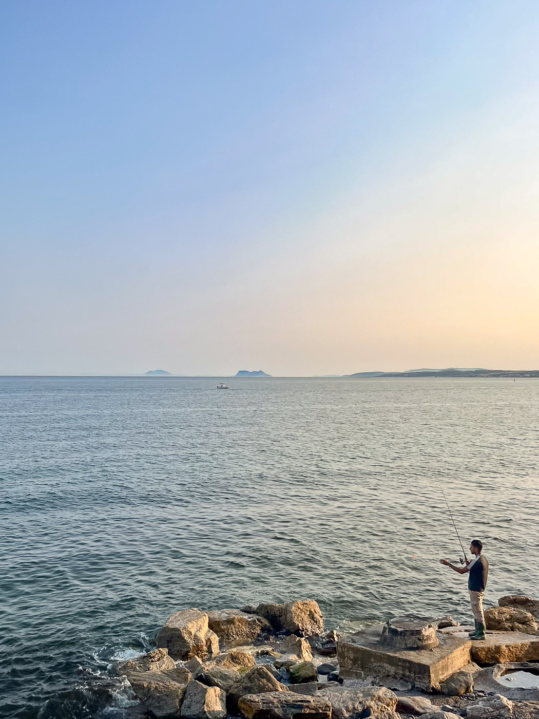 Man fishing at sunset in Estepona with Gibraltar on the horizon